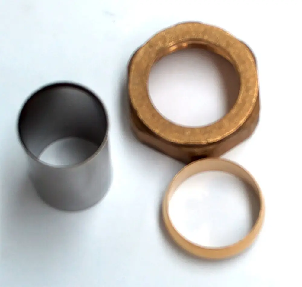 Daikin Zubehör-Set bestehend aus drei metallischen Komponenten: einem zylindrischen Teil, einer sechseckigen Mutter und einem Ring, auf hellem Hintergrund.